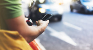 A man using a smartphone at the side of a busy street.